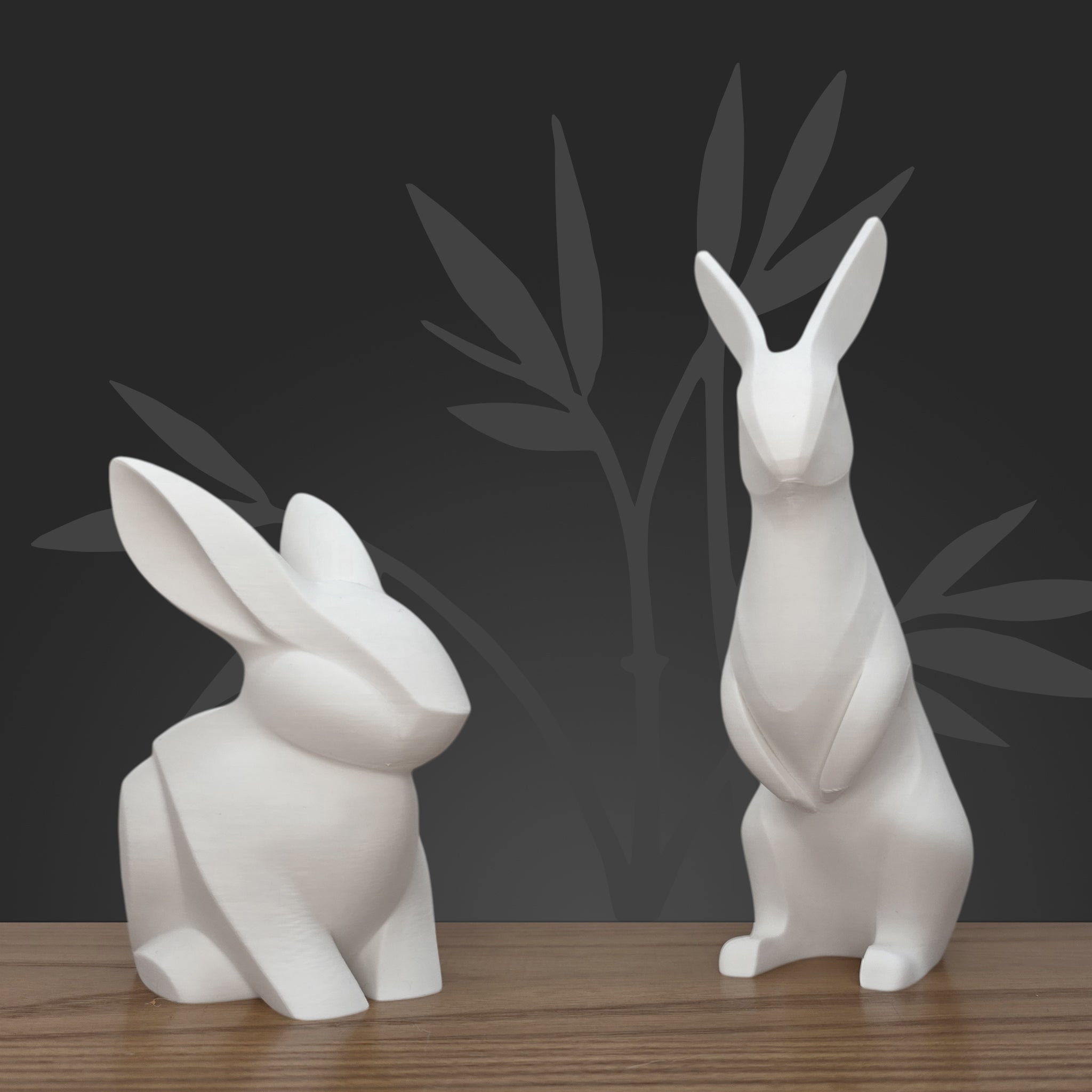 Duo de sculptures lapins minimalistes debout et assis, style origami blanc pur mat, sur table en bois.